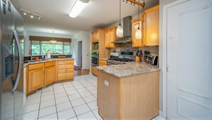 Una cocina moderna con armarios de madera, una isla central, electrodomésticos de acero inoxidable y un amplio ventanal que proporciona luz natural.