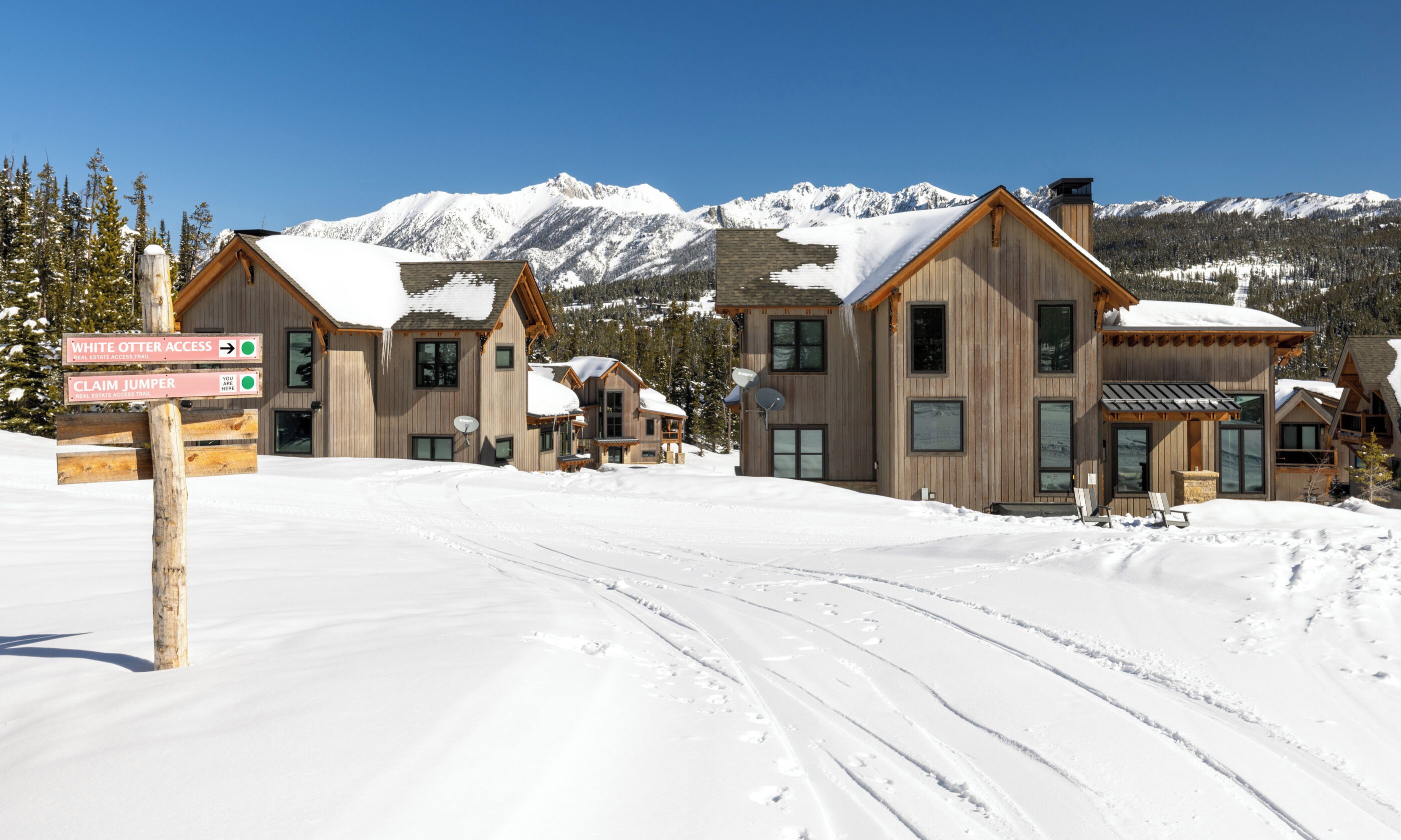 Une station de ski enneigée, avec des chalets en bois et un panneau indiquant l’accès aux pistes White Otter et Claim Jumper.