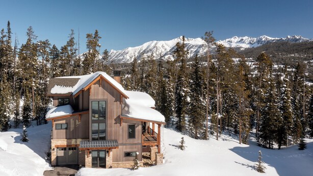 Una baita di legno con un balcone, circondata da alberi innevati e montagne sullo sfondo.