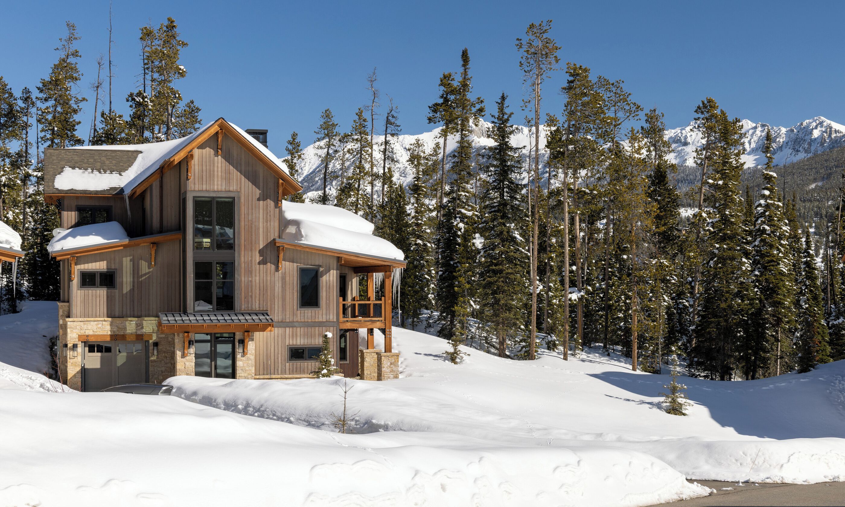 Une cabane en bois à plusieurs étages, dotée d’un balcon, entourée d’arbres et de montagnes couverts de neige.