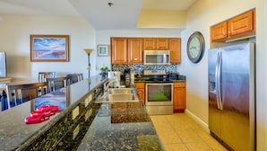 A modern kitchen with granite countertops, stainless steel appliances, wooden cabinets, and a large island with seating. - Ariel Dunes II2306 - 23rd Floor, Breathtaking Views, Accommodates up to 6! (Miramar Beach)