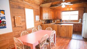 Interior de una cabaña de madera con comedor, cocina y un ventilador de techo.