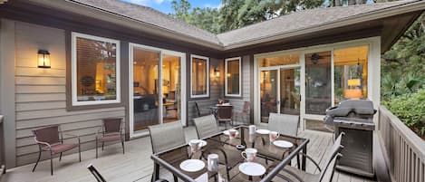 A covered patio with a dining table, chairs, and a grill.