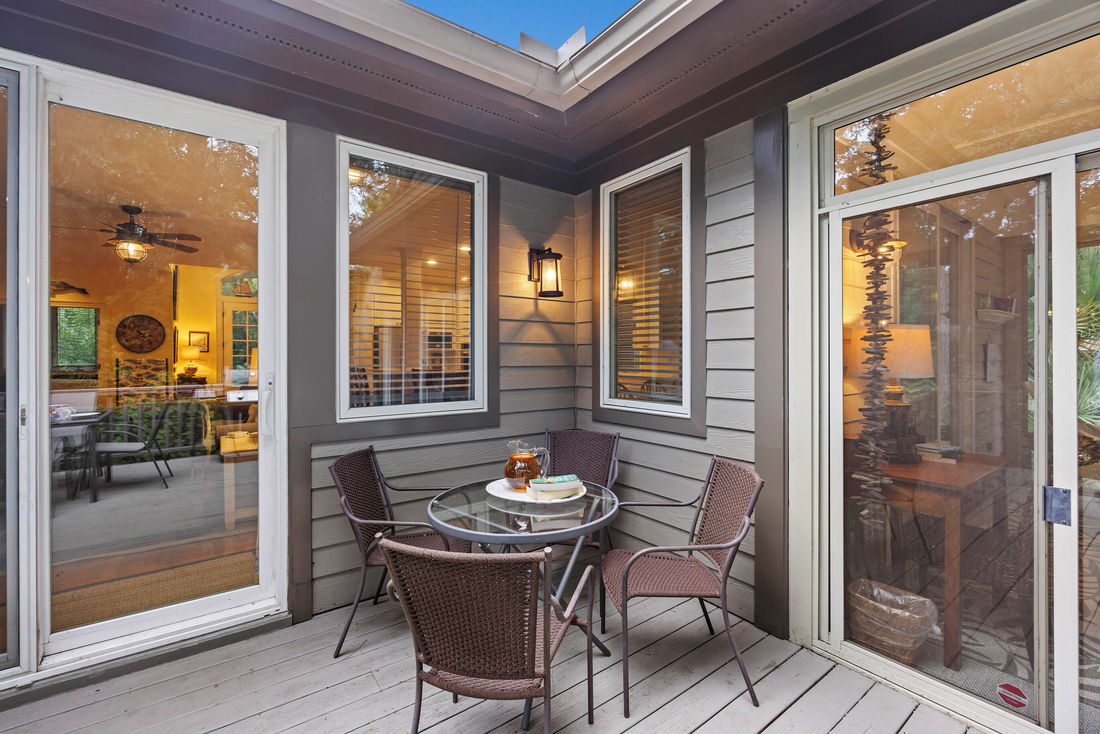 A covered patio with a glass table and wicker chairs, overlooking a dining area.