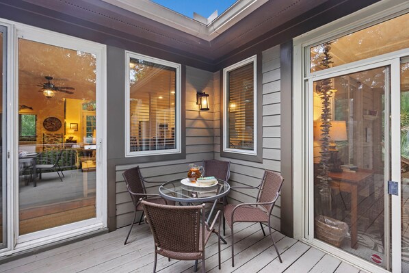 A covered patio with a glass table and wicker chairs, overlooking a dining area.