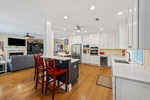 A modern kitchen with white cabinets, a central island with bar stools, a built-in oven, and a large window.