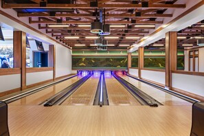 Une salle de bowling avec des poutres en bois, des pistes numérotées et un mur vert orné d’une fresque représentant des poissons.