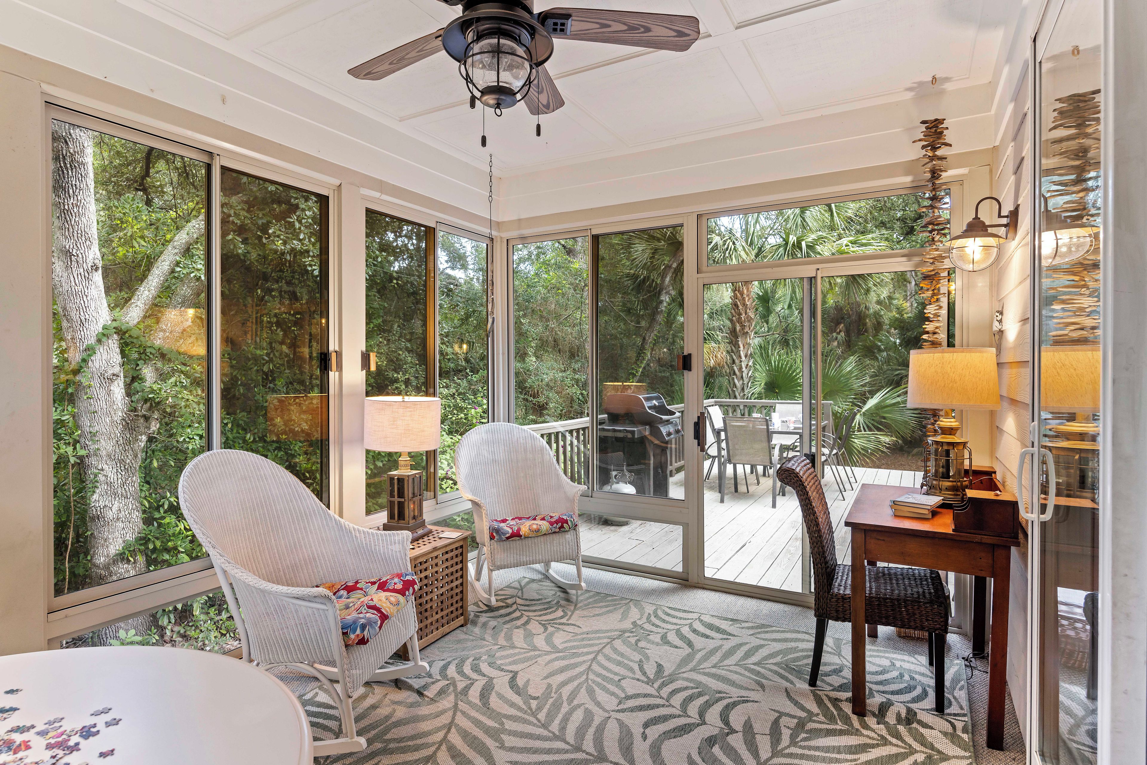 A sunroom with large sliding glass doors, wicker furniture, and a ceiling fan.