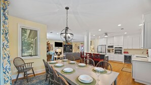 Une cuisine moderne avec des meubles blancs, un coin repas avec une table dressée pour quatre personnes et un salon doté d’une cheminée.