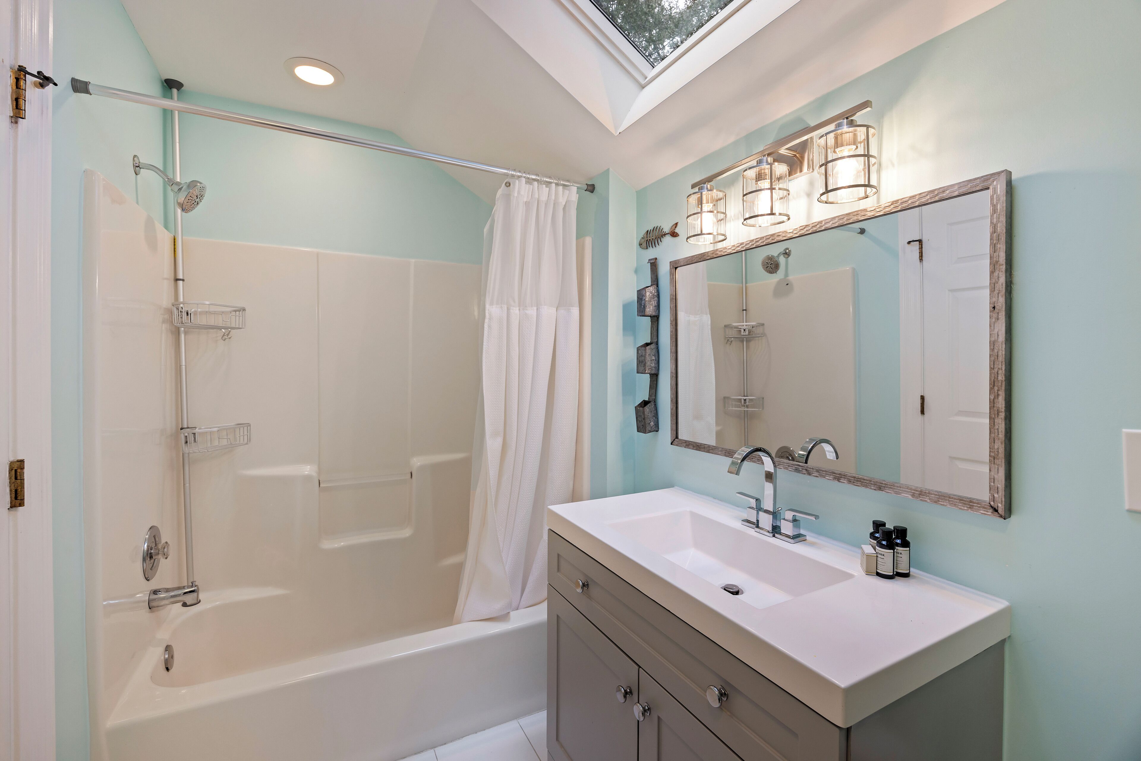 Un baño moderno con tragaluz, bañera, ducha y tocador con espejo.