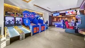 Un espace de jeux équipé de bornes d’arcade de basketball, d’un grand écran de télévision et d’un coin salon avec des fauteuils rouges.