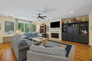 Un salon avec une cheminée, un ventilateur de plafond et un téléviseur.