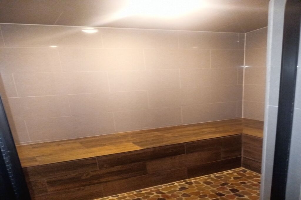 Une salle de bain avec des carreaux de couleur beige, un banc en bois et un sol imitant la pierre.