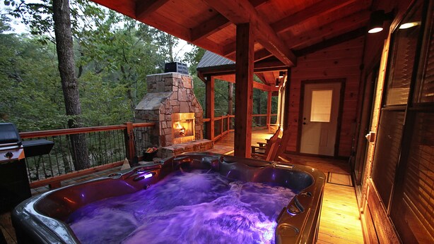 A hot tub with flowing water, surrounded by wooden deck and a stone fireplace.