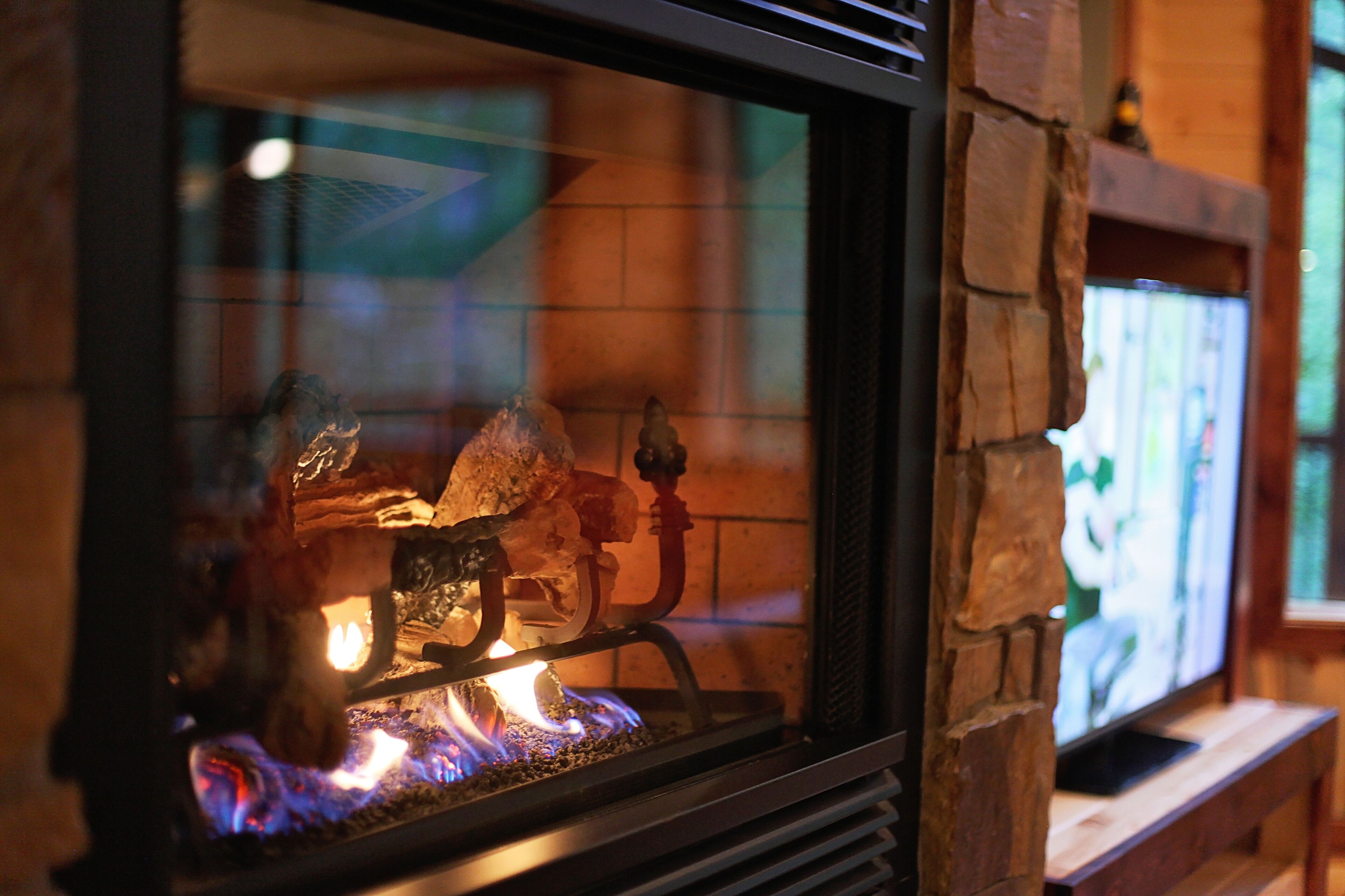 A fireplace with logs and a television set in the background.