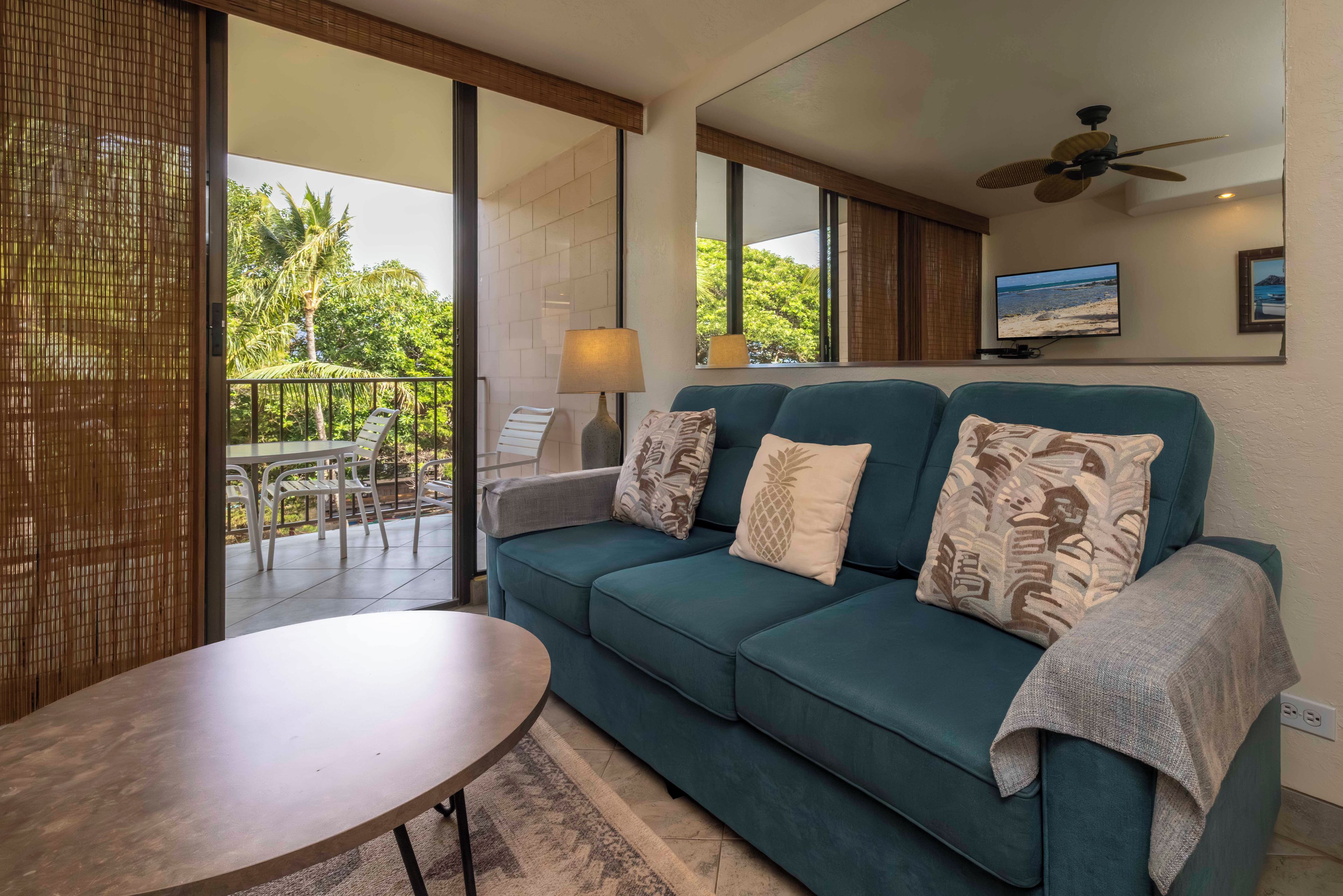 A modern living room with a teal sofa, a round table, and a TV on the wall.