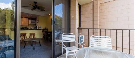 A balcony with a glass door leading to a kitchen area, a white metal table, and two white metal chairs.
