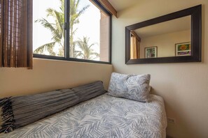 A room with a bed, a window with bamboo curtains, and a wall-mounted mirror. - Kealia 407 Partial Ocean View Comfortable Charming Paradise Unit Washer/Dryer (Kihei)