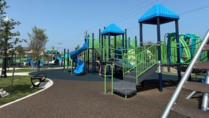 Une aire de jeux dotée de plusieurs toboggans et de structures d’escalade, entourée d’une zone pavée avec des bancs et des arbres.