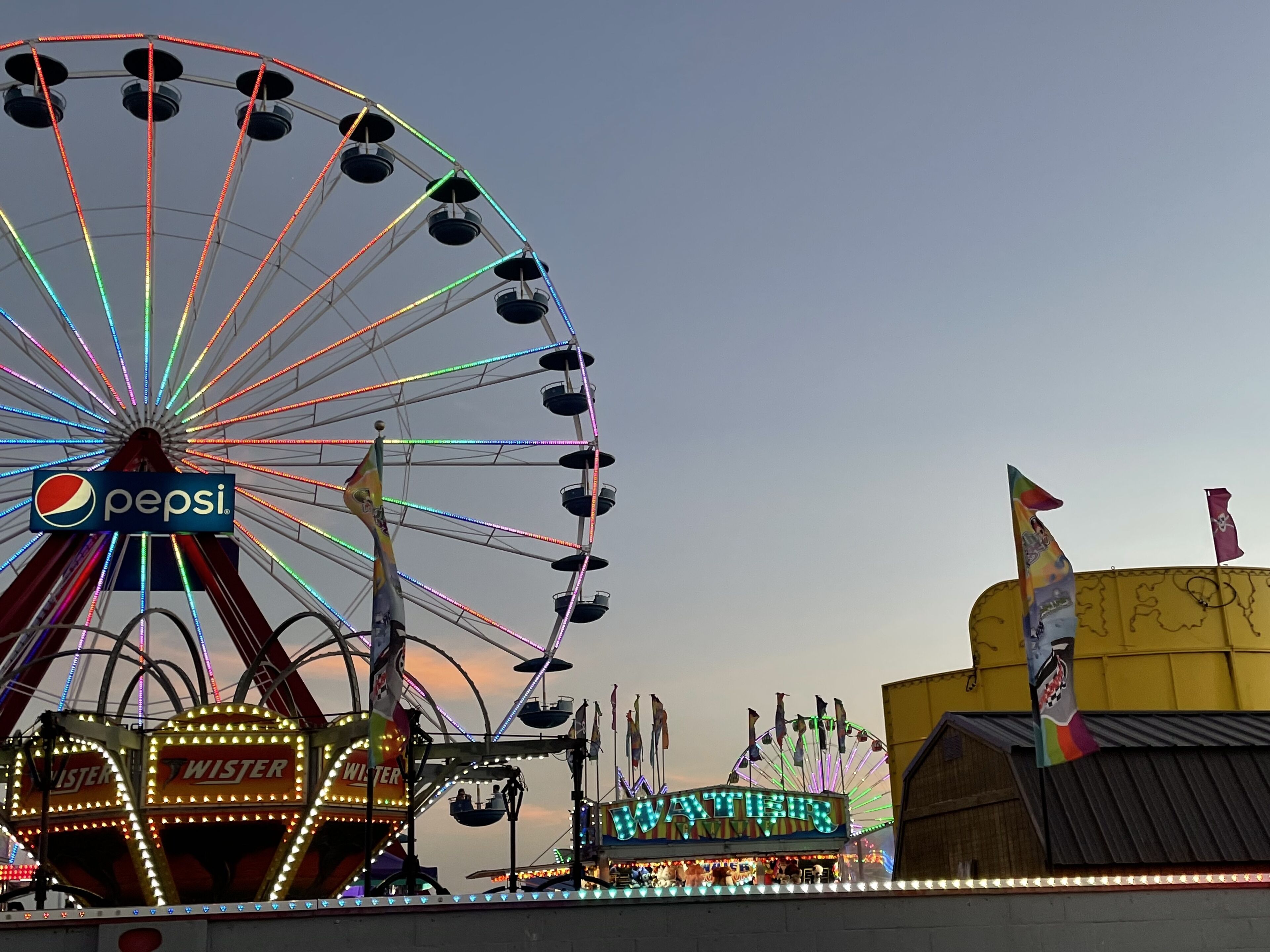 A Ferris wheel with a Pepsi sign, a water ride, and a building with flags.
