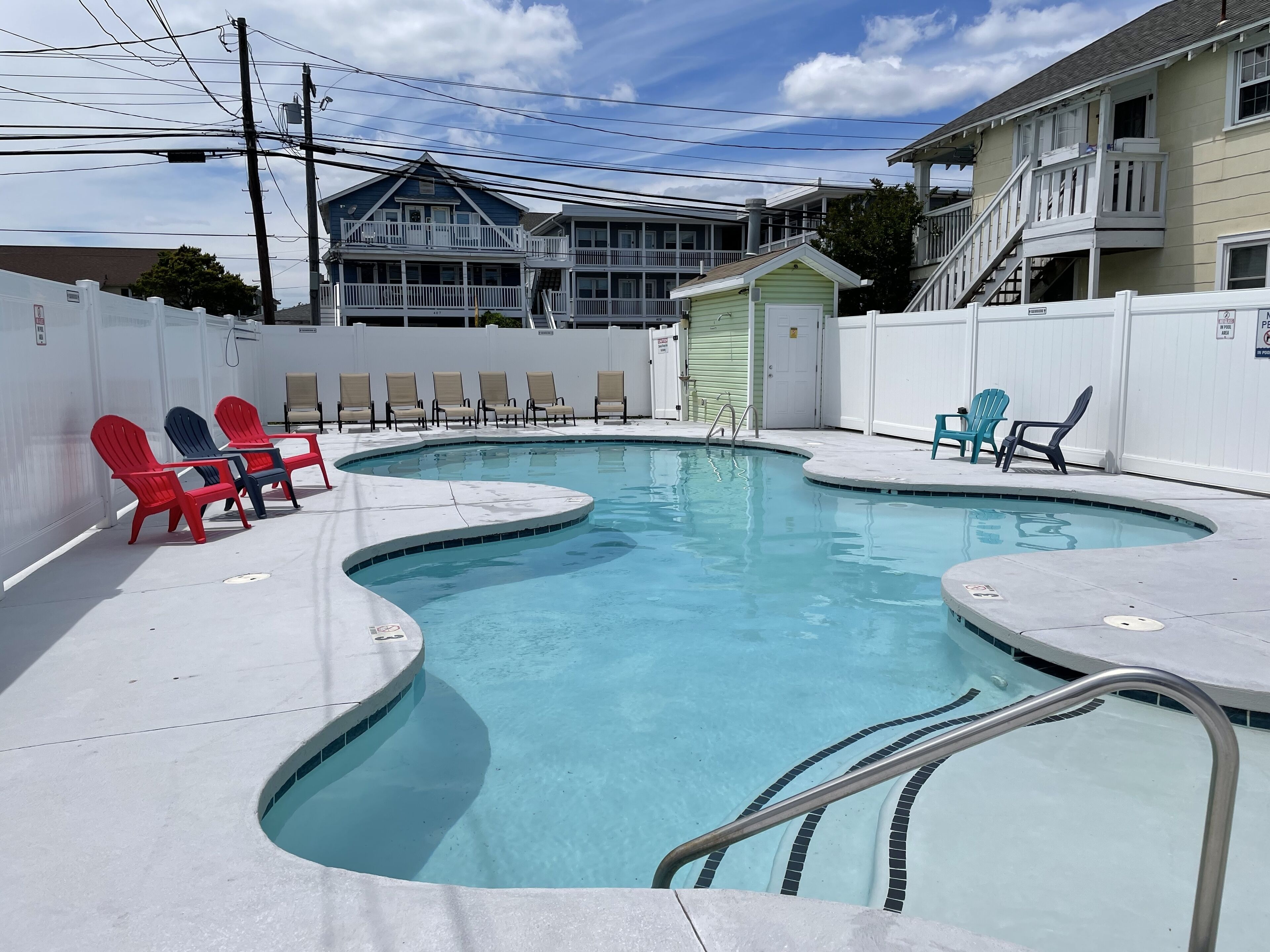 Ein Pool mit geschwungener Kante, umgeben von Liegestühlen und einem kleinen Gebäude.