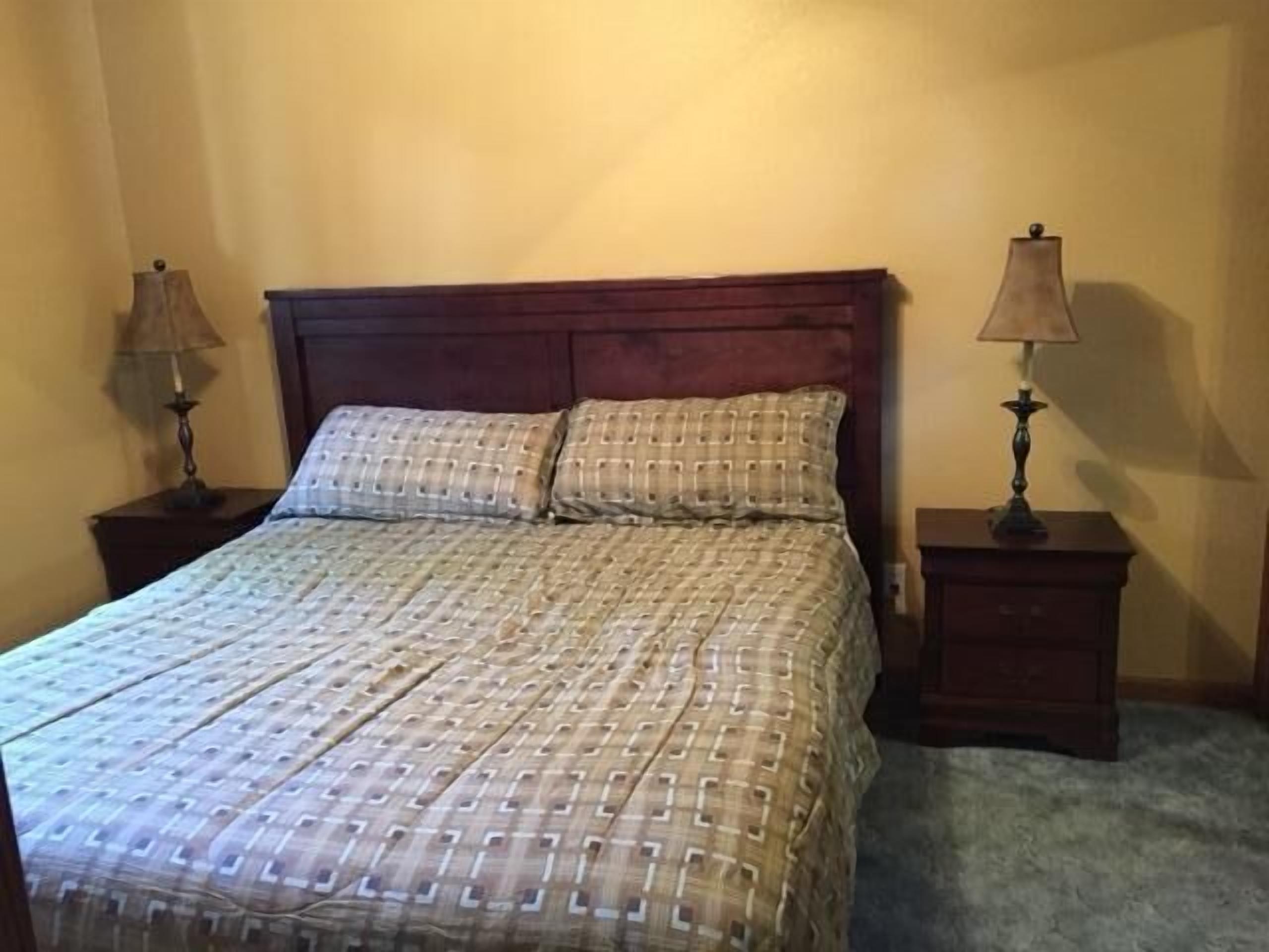Un lit bien fait, recouvert d’une couvre-lit à motifs et agrémenté de deux oreillers, avec deux tables de chevet de chaque côté, sur lesquelles sont posées des lampes.