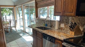 A kitchen with wooden cabinets, a granite countertop, stainless steel appliances, and a large window providing natural light. - Cozy Private Lakefront Cottage Surrounded By Lush Trees (Carnelian Bay)