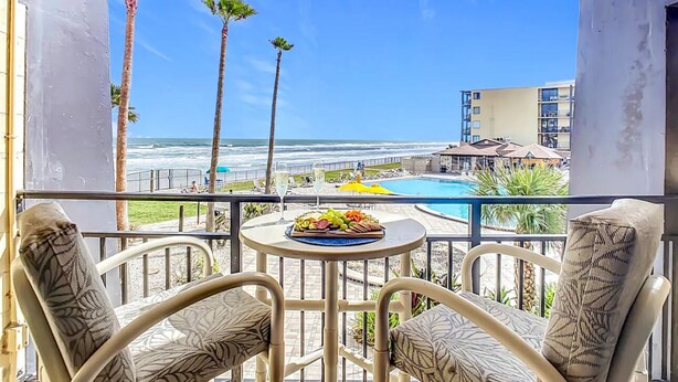 Ein Balkon mit Esstisch, Blick auf Pool und Strand mit Palmen.