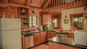Cocina de cabaña de madera con refrigerador, estufa, pileta y alacenas de madera.
