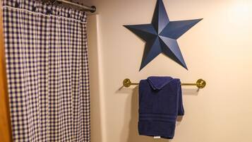 Un baño con cortina de ducha a cuadros, un adorno con forma de estrella en la pared y un perchero con una toalla.