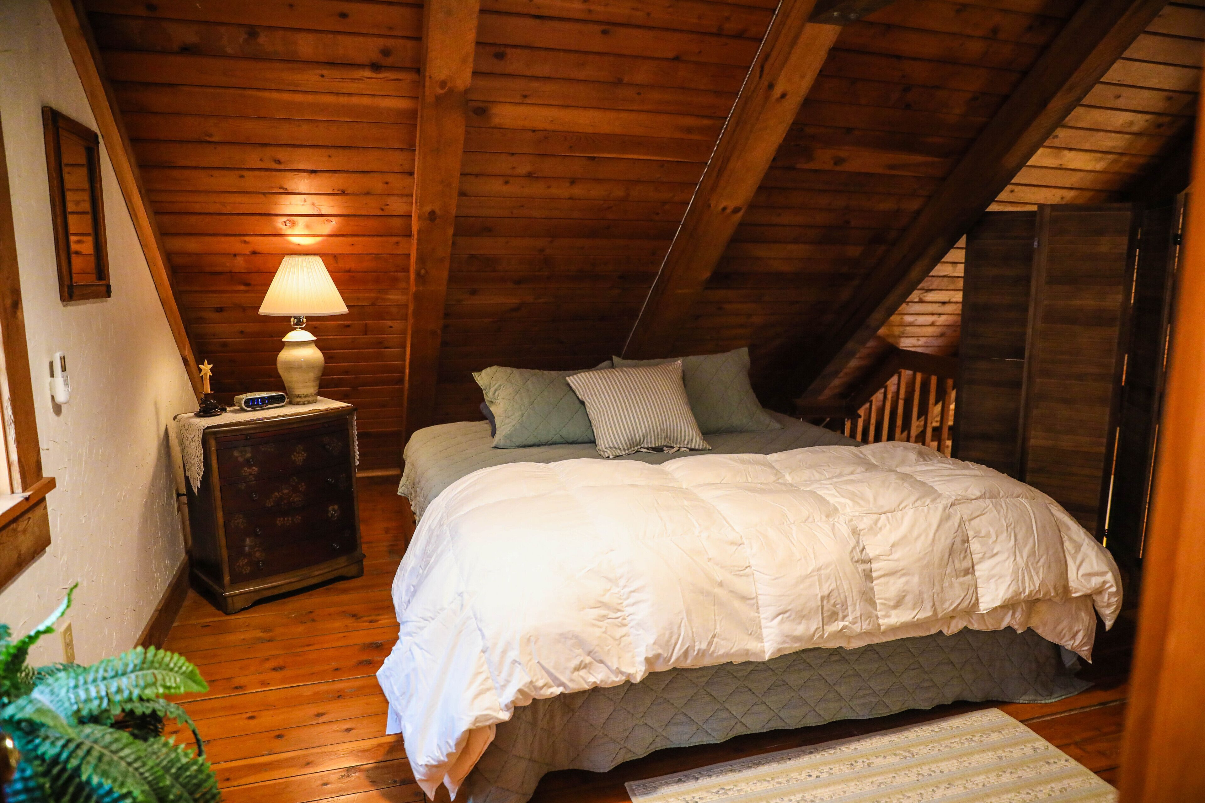A bedroom with a wooden ceiling, a bed with white bedding, a nightstand with a lamp, and a small table with a decorative item.