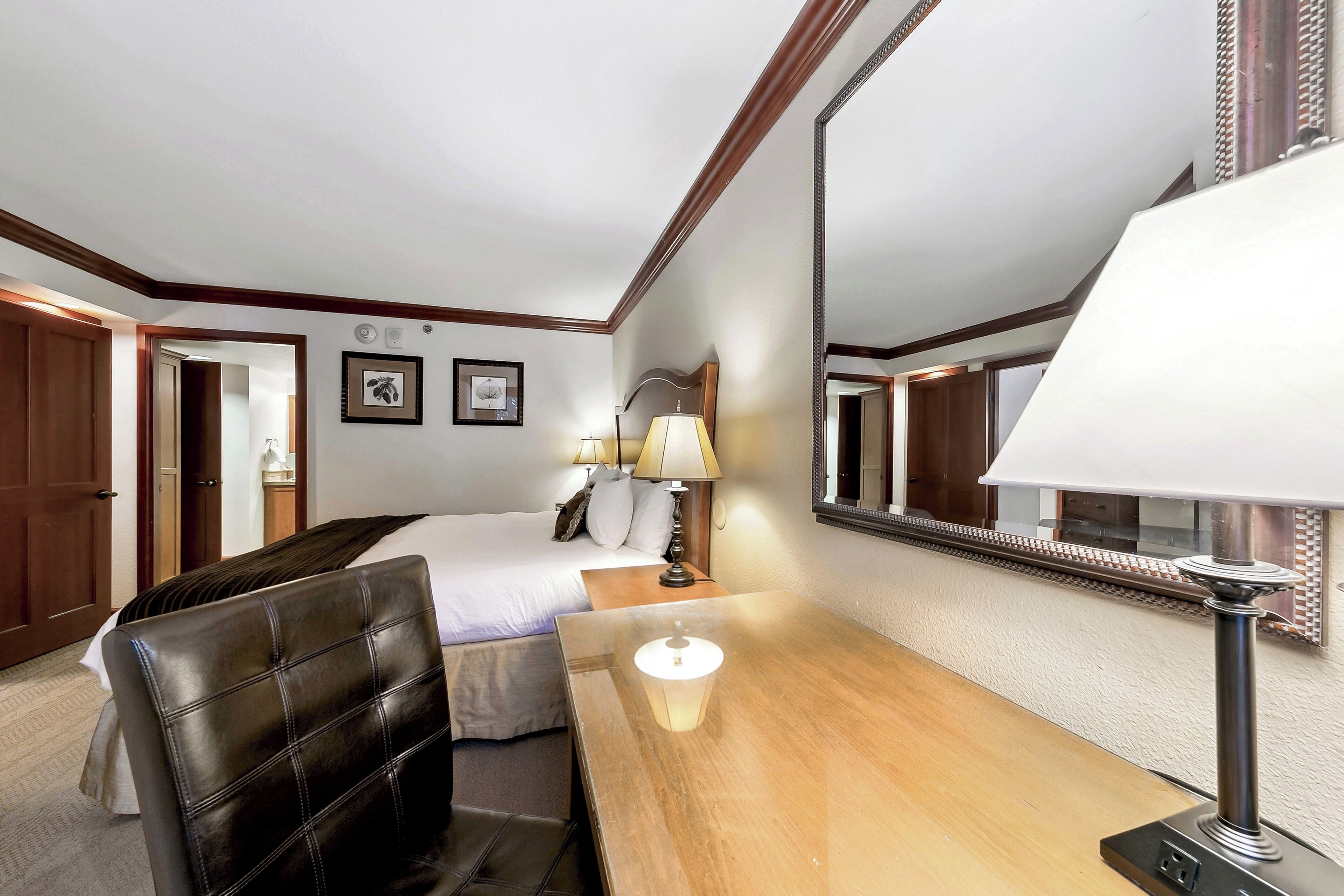 Une chambre d’hôtel avec un lit, un bureau, une chaise, une lampe et un grand miroir.