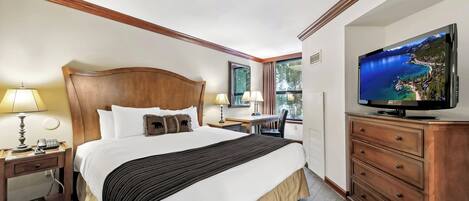A hotel room with a large bed, bedside lamps, a desk with a chair, a television, and a dresser.