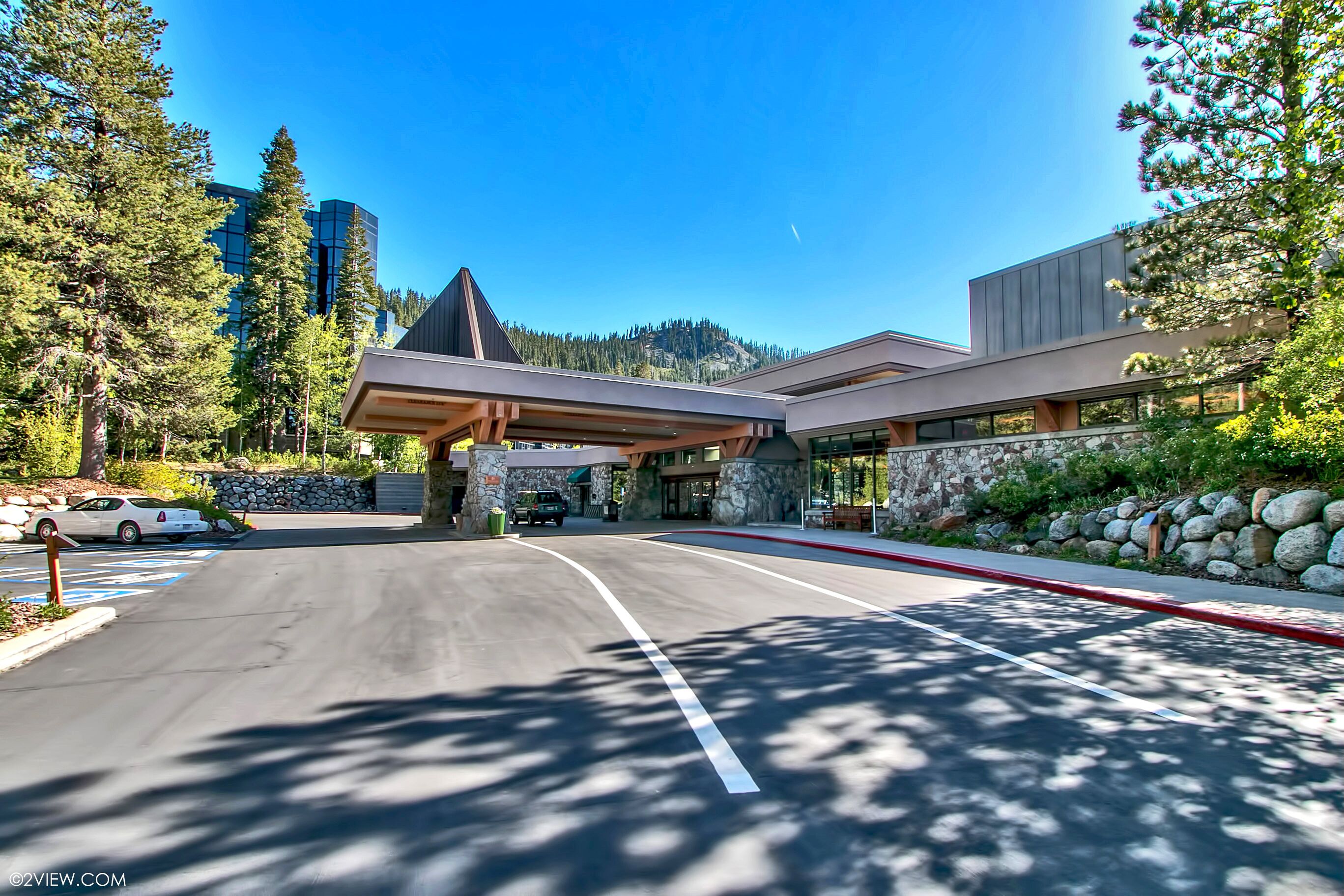 A modern building with a stone facade, a covered entrance, and a parking lot.