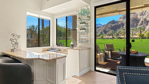 A modern kitchen with a large island, a glass display shelf, and a view of a golf course.