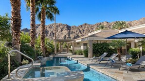 A pool area with lounge chairs, a hot tub, and palm trees.