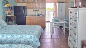 Une chambre compacte comprenant deux lits, un coin cuisine, un espace repas et un ventilateur de plafond.