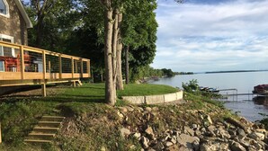 A lakeside property with a wooden deck, stone steps, and a grassy area leading to a dock. - Waterfront Lake House - built in 2017 on shoreline & dog friendly (Swanton)