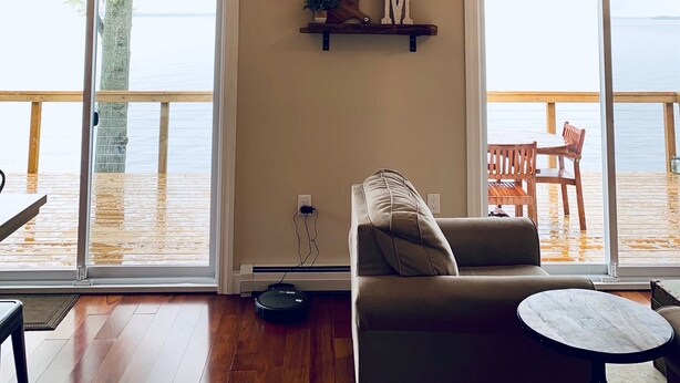 A spacious living room with a large window overlooking a wooden deck. - Waterfront Lake House - built in 2017 on shoreline & dog friendly (Swanton)