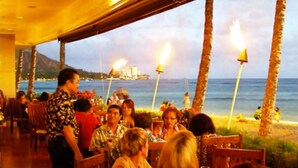 Ein Restaurant mit Außenbereich und Meerblick, das einen Blick auf den Strand und eine entfernte Skyline bietet.