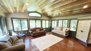 A spacious living room with a wooden ceiling, large windows, a brown leather sofa, a white sofa, and a large rug. - Waterfront in Montana!! Bigfork & Glacier Nat. Park! Aug & Sept is still open!!! (Bigfork)