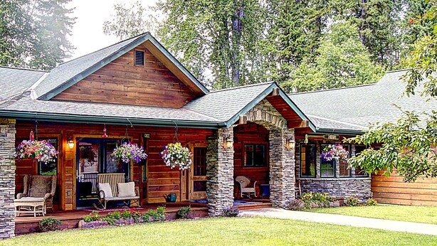 A log cabin with a stone foundation, a porch with wicker furniture, and hanging flower baskets. - Waterfront in Montana!! Bigfork & Glacier Nat. Park! Aug & Sept is still open!!! (Bigfork)