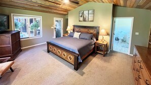 A bedroom with a wooden ceiling, a bed with a headboard, two bedside tables with lamps, and a view of the outside through a window. - Waterfront in Montana!! Bigfork & Glacier Nat. Park! Aug & Sept is still open!!! (Bigfork)
