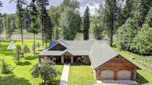 A log cabin with a garage, surrounded by a grassy yard and trees. - Waterfront in Montana!! Bigfork & Glacier Nat. Park! Aug & Sept is still open!!! (Bigfork)