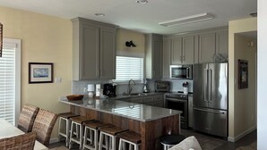 A modern kitchen with grey cabinets, stainless steel appliances, and a bar area with stools. - Beautiful Gulf-Front Duplex  in Morgantown. Gulf Shores, AL (Gulf Shores)