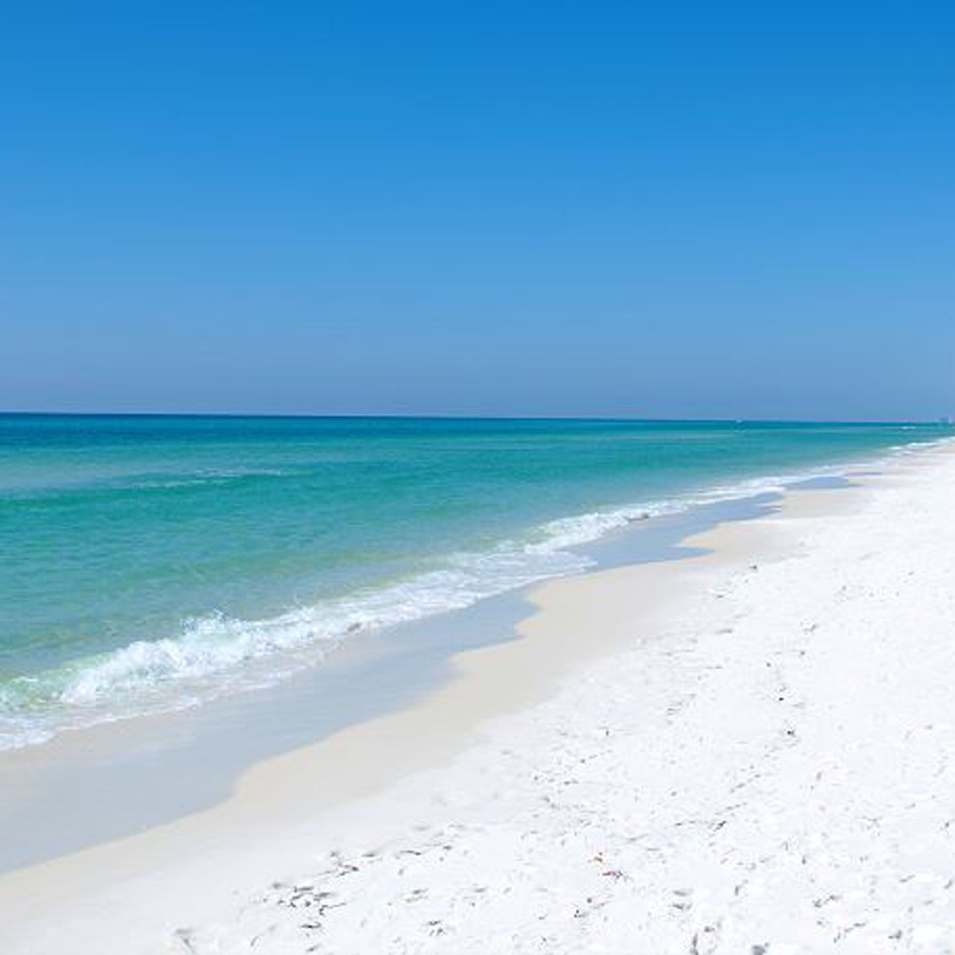 En strand med kristallklart, turkosfärgat vatten och vit sand.