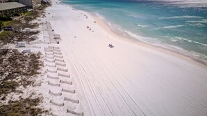 En strand med en lång sträcka vit sand, några parasoller och några få personer. I bakgrunden syns några byggnader.