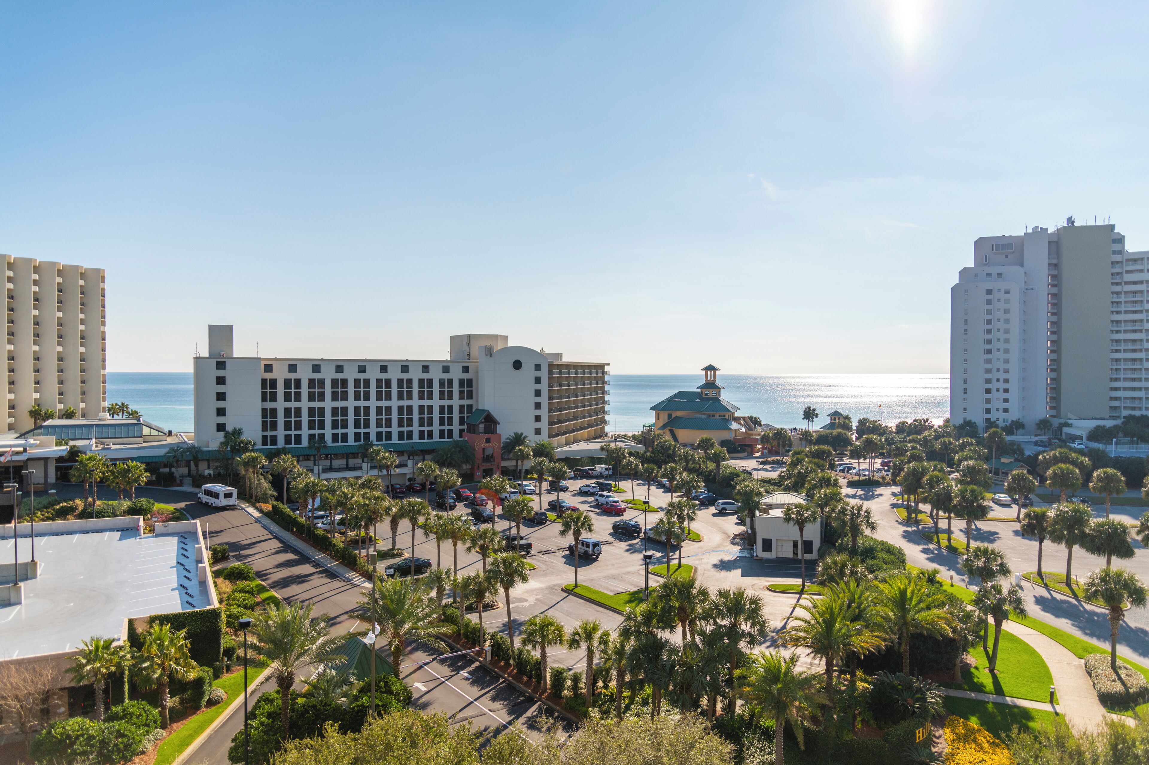 A hotel with a parking lot, palm trees, and a view of the ocean.
