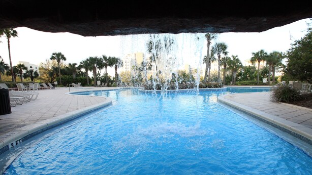 Una piscina con fuente, rodeada de tumbonas y palmeras.