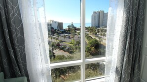 Vista a través de una ventana con cortinas translúcidas, mostrando un paisaje urbano con edificios, un estacionamiento y cielo despejado.